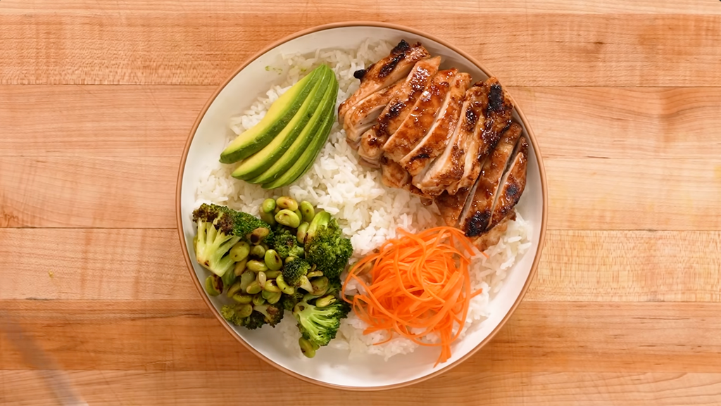High protein chicken bowl with grilled chicken breast, quinoa, broccoli, tomatoes, cucumber, red cabbage and avocado.